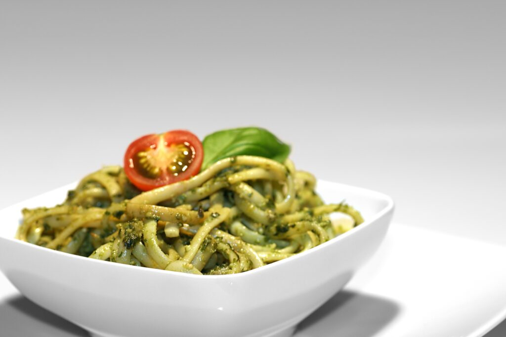 Nudeln mit Basilikumpesto und Tomate in einer weißen Schüssel,